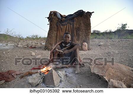 "Young shepherdess from the Himba people sitting at a campfire in front of her hut, Ombombo, Kaokoland, Kunene, Namibia, Africa" View Large Photo Image Stock Image - "Young shepherdess from the Himba people sitting at a campfire in front of her hut, Ombombo, Kaokoland, Kunene, Namibia, Africa". Fotosearch