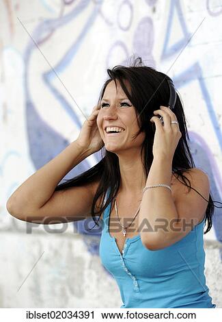 Stock Image - Young smiling woman listening to music with headphones in front of graffiti. Fotosearch