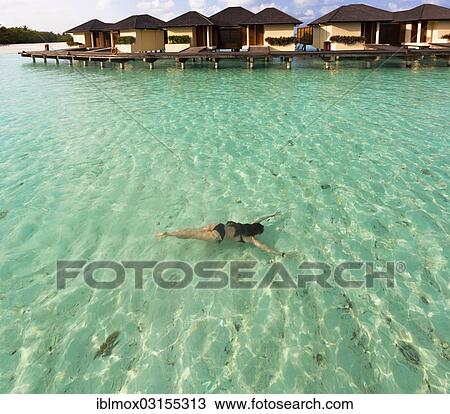 Stock Image - "Young woman, about 19 years, swimming under water in a lagoon, the water bungalows of Paradise Iceland at the back, Indian Ocean, Lankanfinolhu, North Male Atoll, Maldives, Asia". Fotosearch