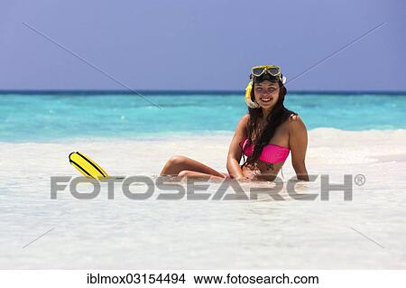 Picture - "Young woman, about 20, sitting on a sandbank with snorkeling gear, Indian Ocean, Male, North Male Atoll, Maldives, Asia". Fotosearch