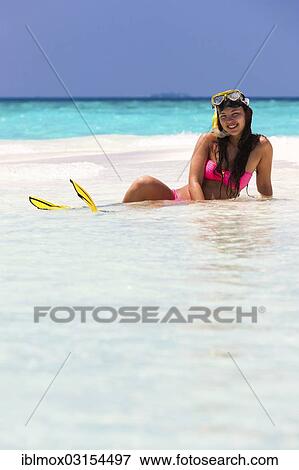 Stock Photo - "Young woman, about 20, sitting on a sandbank with snorkeling gear, Indian Ocean, Male, North Male Atoll, Maldives, Asia". Fotosearch