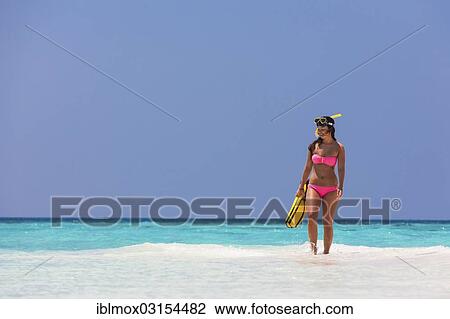 Stock Image - "Young woman, about 20, walking over a sandbank with snorkeling gear, Indian Ocean, Male, North Male Atoll, Maldives, Asia". Fotosearch
