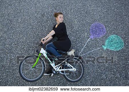 "Young woman appearing to cycle on a children's bicycle, painted balloons tied to the rack, taken from above" View Large Photo Image Stock Photo - "Young woman appearing to cycle on a children's bicycle, painted balloons tied to the rack, taken from above". Fotosearch