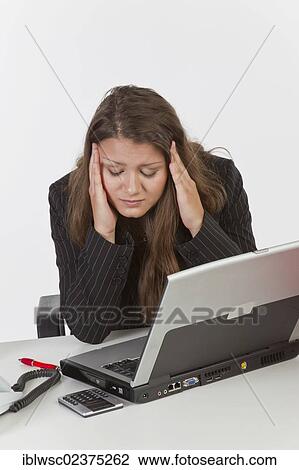 Stock Image - "Young woman at her desk with a laptop computer, headache". Fotosearch