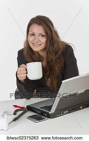 Young woman at her desk with a laptop computer holding a cup of coffee View Large Photo Image Stock Image - Young woman at her desk with a laptop computer holding a cup of coffee. Fotosearch