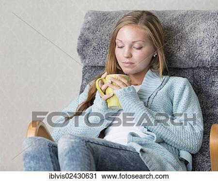 Stock Image - "Young woman at home, relaxing, holding a mug". Fotosearch