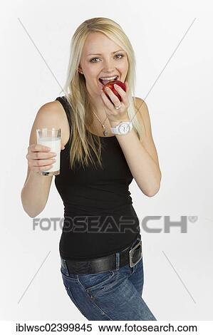 Young woman biting into an apple whilst holding a glass of milk View Large Photo Image Stock Photography - Young woman biting into an apple whilst holding a glass of milk. Fotosearch