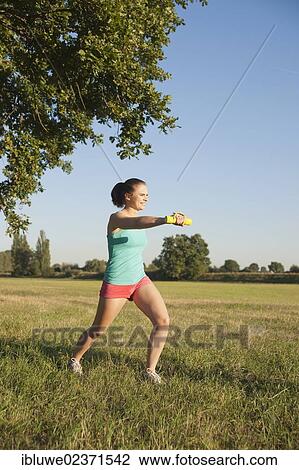 Young woman doing dumbbell exercises in a meadow View Large Photo Image Stock Image - Young woman doing dumbbell exercises in a meadow. Fotosearch