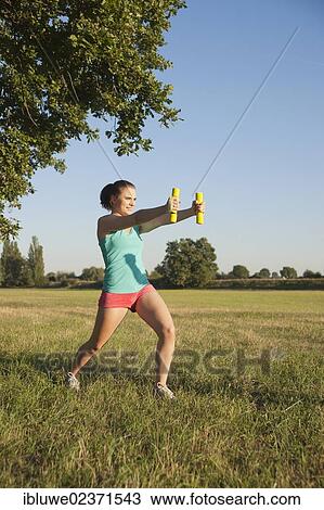 Young woman doing dumbbell exercises in a meadow View Large Photo Image Stock Image - Young woman doing dumbbell exercises in a meadow. Fotosearch