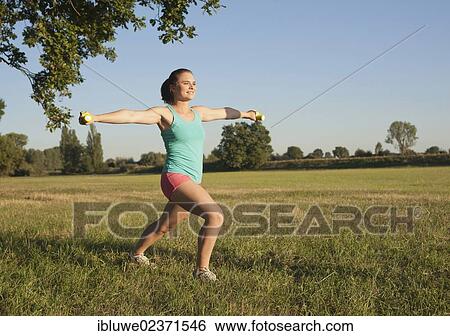 Young woman doing dumbbell exercises in a meadow View Large Photo Image Stock Photograph - Young woman doing dumbbell exercises in a meadow. Fotosearch