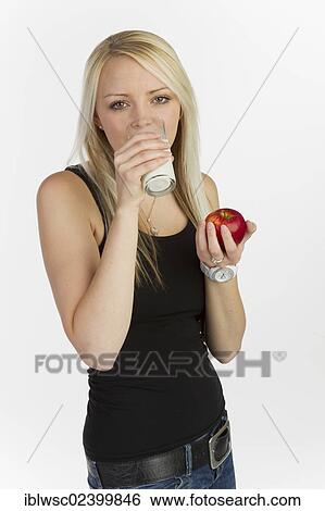 Young woman drinking a glass of milk whilst holding an apple View Large Photo Image Stock Photograph - Young woman drinking a glass of milk whilst holding an apple. Fotosearch