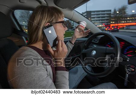 Young woman driving a car in the city centre while talking on her cell phone and holding a cup of coffee at the same time View Large Photo Image Stock Image - Young woman driving a car in the city centre while talking on her cell phone and holding a cup of coffee at the same time. Fotosearch