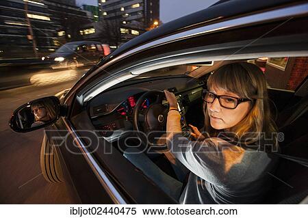 Stock Photography - Young woman driving a car in the city centre at night. Fotosearch