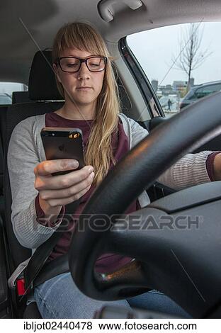 Stock Photo - Young woman driving a car while texting on her cell phone. Fotosearch