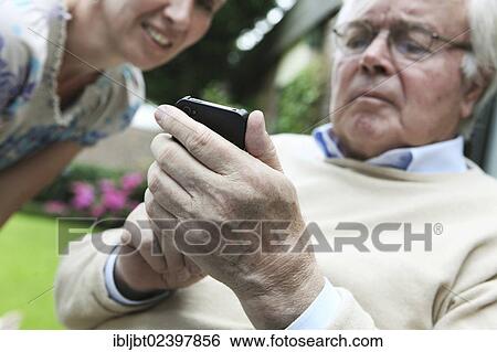 Stock Photograph - Young woman explaining to a senior citizen how to use a smartphone. Fotosearch