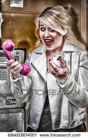 Stock Image - Young woman having to choose between a mobile phone and a phone booth. Fotosearch