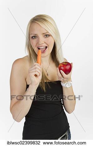 Stock Image - Young woman holding a carrot and an apple in her hands. Fotosearch