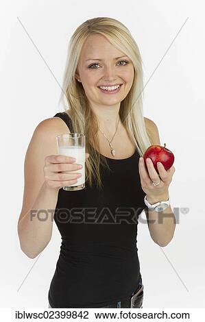 Stock Image - Young woman holding a glass of milk and an apple. Fotosearch