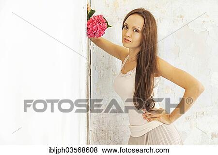 Stock Photo - "Young woman holding a hydrangea, standing at a wall with peeling paint, Germany, Europe". Fotosearch