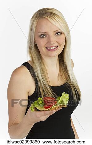 Stock Image - "Young woman holding a slice of bread with grains, topped with cheese and tomato". Fotosearch