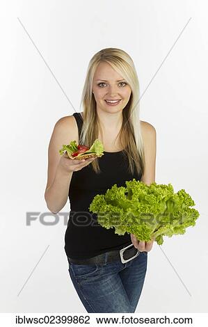"Young woman holding a slice of bread with grains, topped with cheese and tomato, holding a head of lettuce in her hand" View Large Photo Image Stock Image - "Young woman holding a slice of bread with grains, topped with cheese and tomato, holding a head of lettuce in her hand". Fotosearch