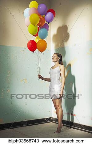 Stock Image - "Young woman holding balloons in a empty room, Germany, Europe". Fotosearch