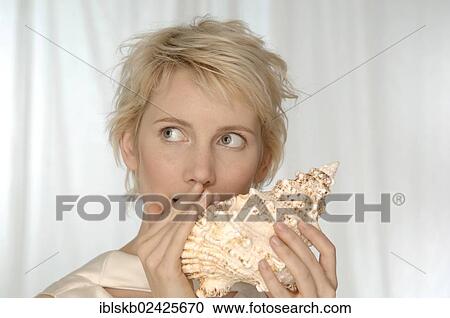 Stock Image - "Young woman holding large shell to her mouth, speaking into it". Fotosearch