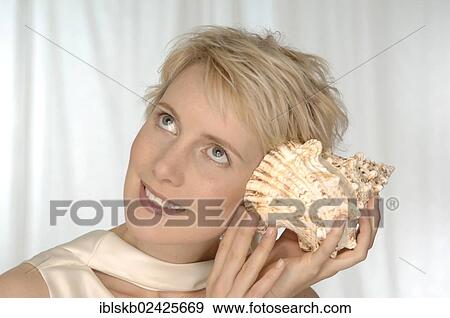 Stock Photo - "Young woman holding large shell to her ear, listening". Fotosearch