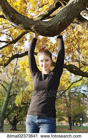 Stock Image - Young woman holding on to a tree branch. Fotosearch