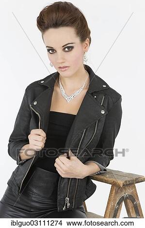 Picture - Young woman in a black leather outfit posing with an old wooden ladder. Fotosearch