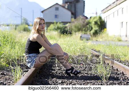 "Young woman in a black top, jeans hot pants and high heels posing sitting on railway tracks" View Large Photo Image Stock Image - "Young woman in a black top, jeans hot pants and high heels posing sitting on railway tracks". Fotosearch
