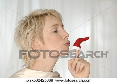 Stock Photo - Young woman kissing miniature Santa hat on her finger. Fotosearch