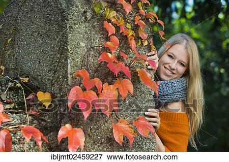 Young woman looking from behind a wall with colorful autumn leaves View Large Photo Image Stock Photo - Young woman looking from behind a wall with colorful autumn leaves. Fotosearch