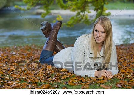 Young woman lying on her belly on the ground in a park View Large Photo Image Stock Photo - Young woman lying on her belly on the ground in a park. Fotosearch