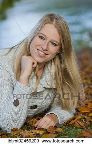 Stock Photo - Young woman lying on her belly on the ground in a park. Fotosearch