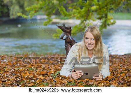 Young woman lying on her belly on the ground in a park and looking at a tablet PC View Large Photo Image Stock Photography - Young woman lying on her belly on the ground in a park and looking at a tablet PC. Fotosearch