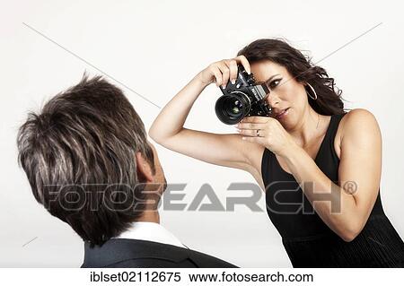 Stock Photography - Young woman photographing a man with an old analog Nikon camera. Fotosearch