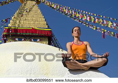 Stock Image - "Young woman practicing yoga at Boudnanath stupa, showing the Padmasana pose, or Lotus pose, Kathmandu Valley, Kathmandu, Kathmandu District, Bagmati Zone, Nepal, Asia". Fotosearch