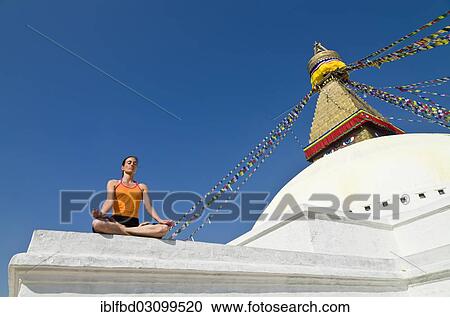 Stock Image - "Young woman practicing yoga at the Boudhanath stupa, showing the Padmasana pose, or Lotus pose, Kathmandu Valley, Kathmandu, Kathmandu District, Bagmati Zone, Nepal, Asia". Fotosearch