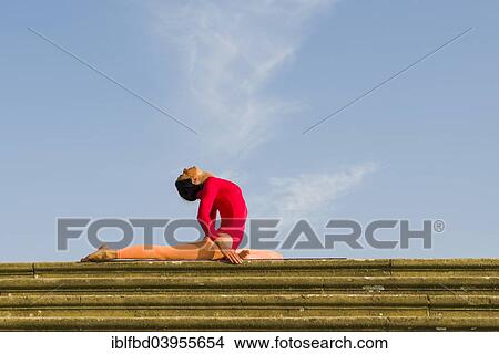 Picture - "Young woman practising Hatha yoga, outdoors, showing the pose Kapotasana, Pigeon pose". Fotosearch