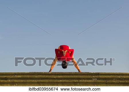Picture - "Young woman practising Hatha yoga, outdoors, showing the pose Prasarita Padottanasana, wide legged forward bend". Fotosearch