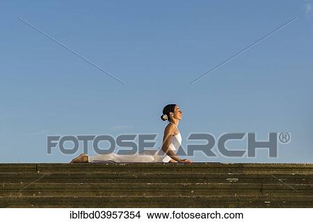 Picture - "Young woman practising Hatha yoga, outdoors, showing the pose Bhujangasana, Cobra pose". Fotosearch