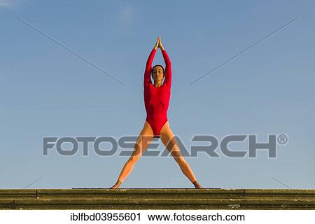 Stock Image - "Young woman practising Hatha yoga, outdoors, showing the pose Tadasana, Mountain pose, with legs apart". Fotosearch