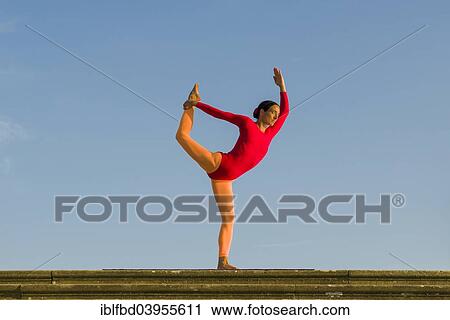 Stock Image - "Young woman practising Hatha yoga, outdoors, showing the pose Saral Natarajasana, preparatory Lord Shiva's pose". Fotosearch