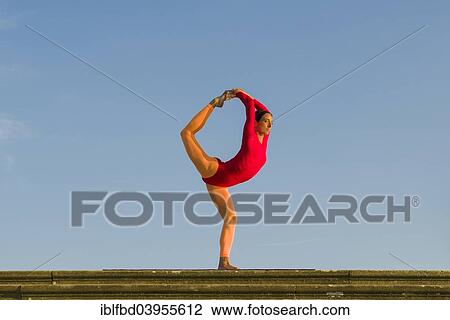 Stock Image - "Young woman practising Hatha yoga, outdoors, showing the pose Natarajasana, Lord Shiva's pose". Fotosearch