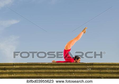Stock Image - "Young woman practising Hatha yoga, outdoors, showing the pose Shalabhasana, Locust". Fotosearch
