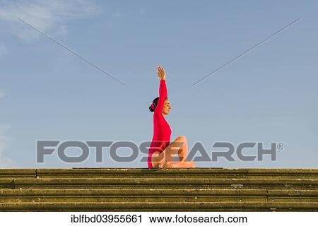 Stock Image - "Young woman practising Hatha yoga, outdoors, showing the pose Ardha Matsyendrasana, half spinal twist". Fotosearch