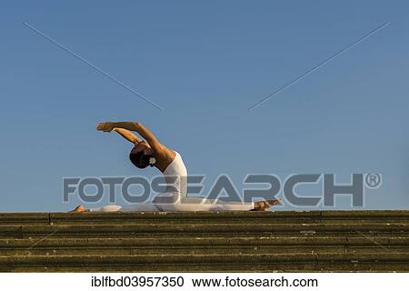 Stock Image - "Young woman practising Hatha yoga, outdoors, showing the pose Anjaneyasana, Hanumanasana, Split". Fotosearch