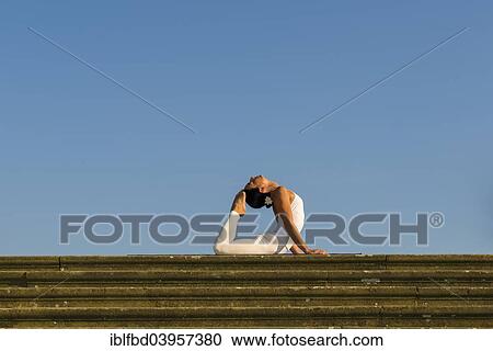 Stock Image - "Young woman practising Hatha yoga, outdoors, showing the pose Bhujangasana, Cobra pose". Fotosearch