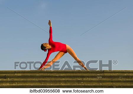 Stock Photo - "Young woman practising Hatha yoga, outdoors, showing the pose Trikonasana, Triangle". Fotosearch